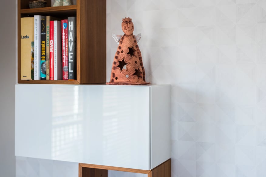 Minimalistický interiér s knihovnou, bílou skříňkou a andělem.